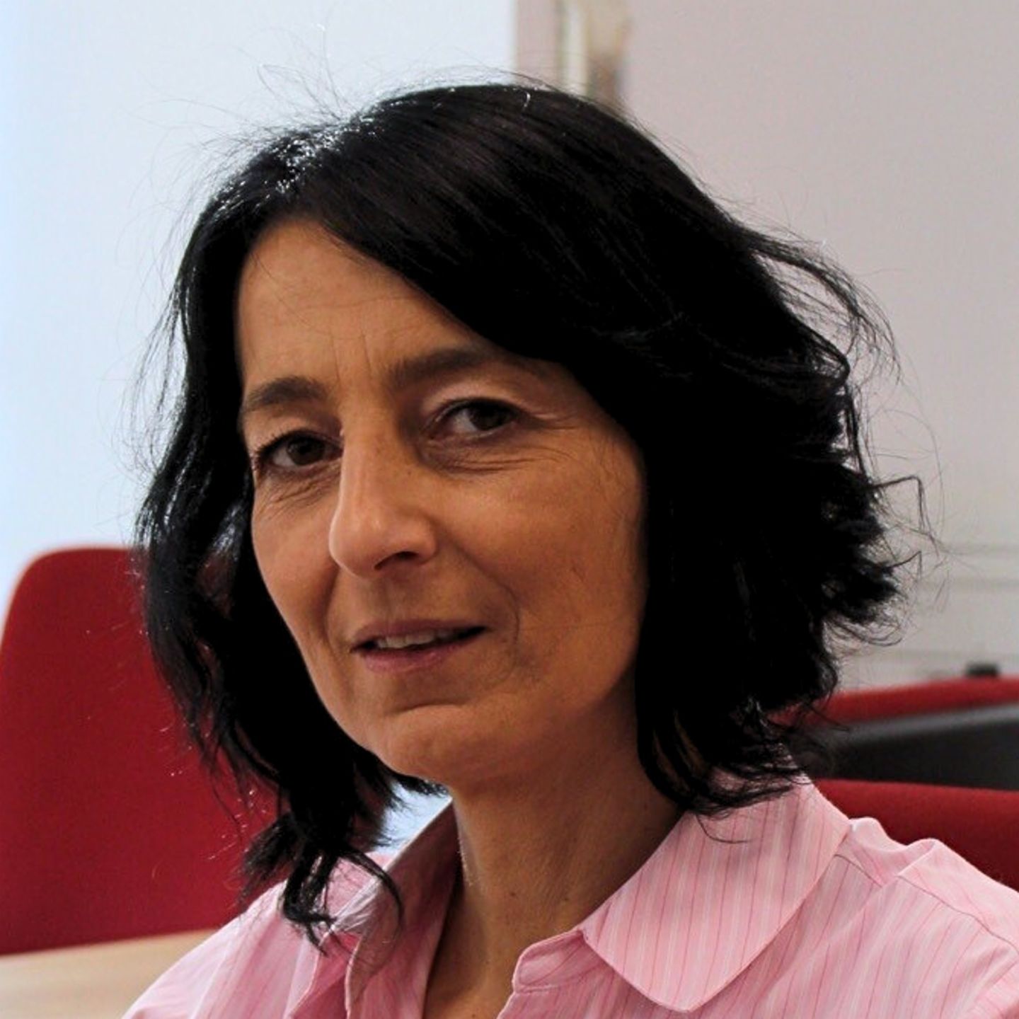 Cristina Pasere, manažérka podpory prevádzky dodržiavania predpisov v EOS Romania, sedí za stolom v ružovej pásikavej blúzke a pozerá do kamery.
