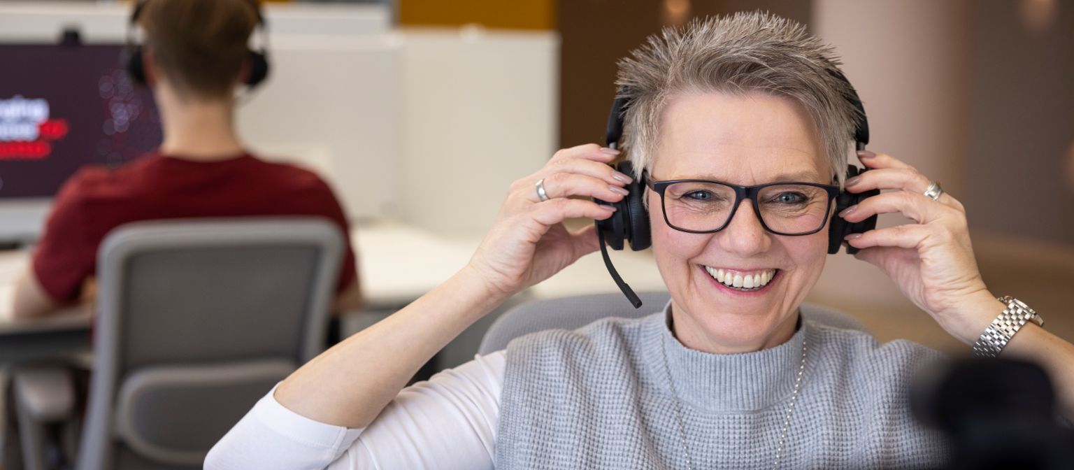 An EOS employee actively participates in a discussion while wearing headphones, with a colleague focused on their computer in the background.