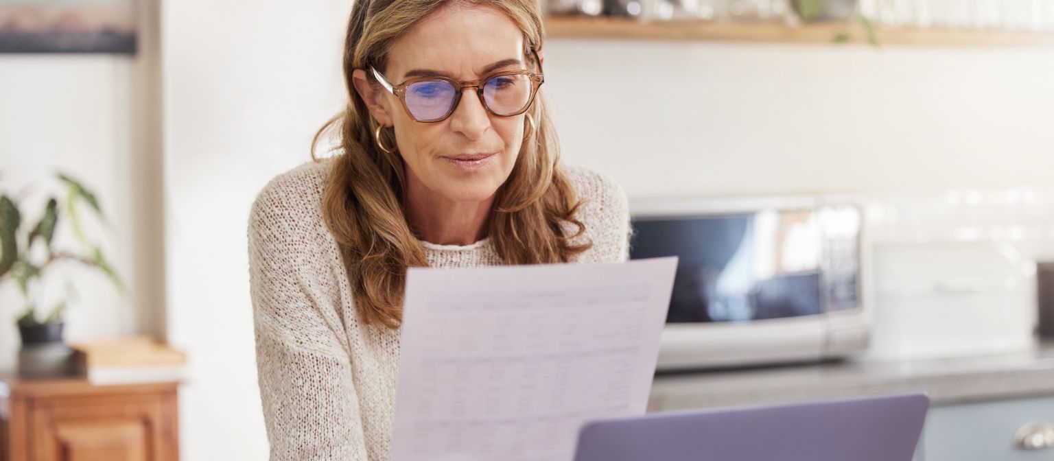 Woman with laptop and paperwork for bills. Elderly person with financial document.