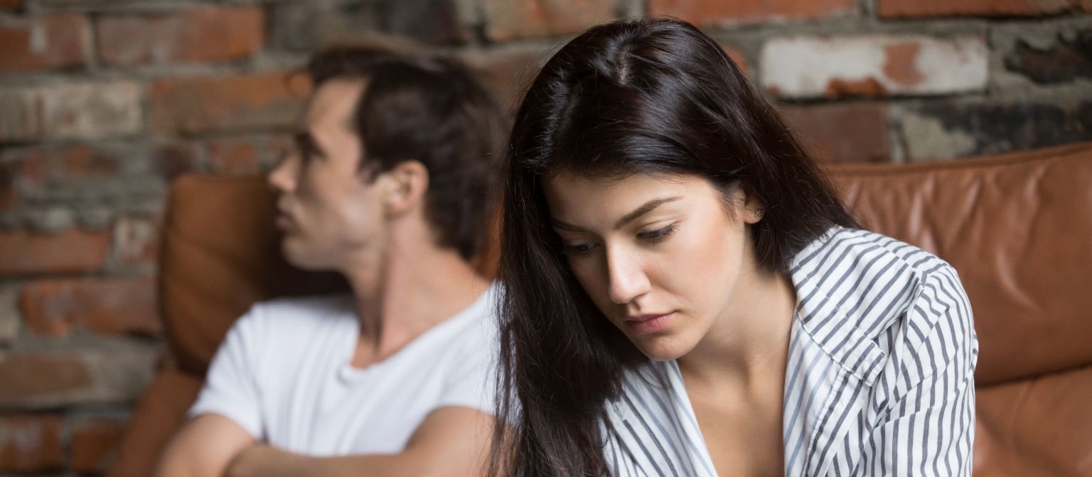 Stressed woman with financial worries sitting thoughtfully while man appears blurred in background - symbolic image of relationship problems due to debt