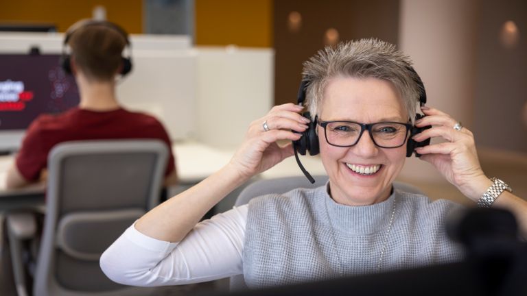 An EOS employee actively participates in a discussion while wearing headphones, with a colleague focused on their computer in the background.