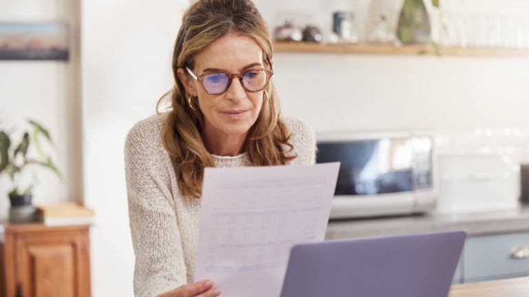 Woman with laptop and paperwork for bills. Elderly person with financial document.