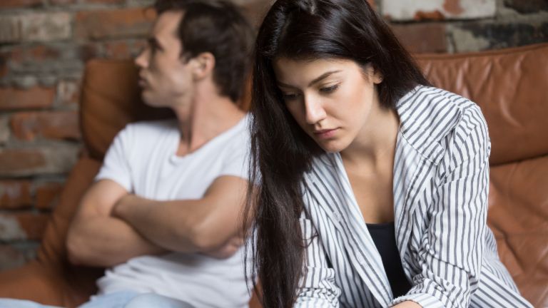Stressed woman with financial worries sitting thoughtfully while man appears blurred in background - symbolic image of relationship problems due to debt