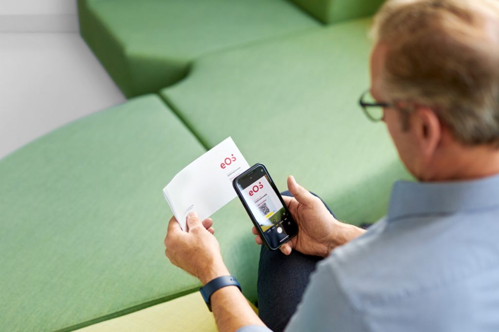Muž skenuje QR kód na liste od EOS so svojím smartfónom, aby uhradil svoju otvorenú pohľadávku online na portáli EOS.