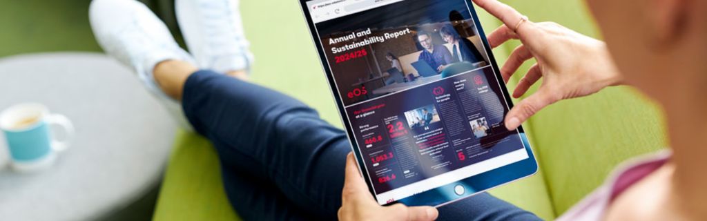 Osoba na zelenej pohovke prezerajúca si Výročnú správu a Správu o udržateľnosti EOS 2024/25 na tablete