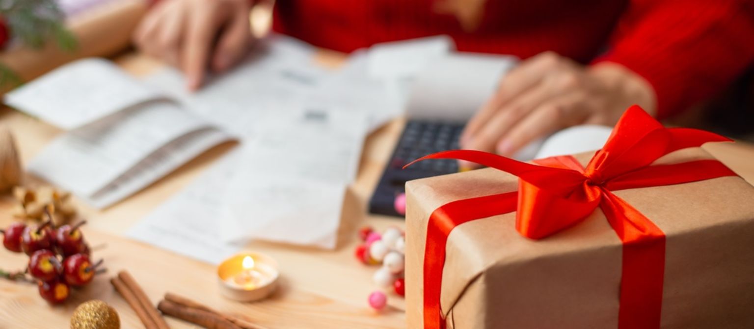 Invoices lay besides Christmas presents at the table. A person sits in front of the table with a red sweater. 