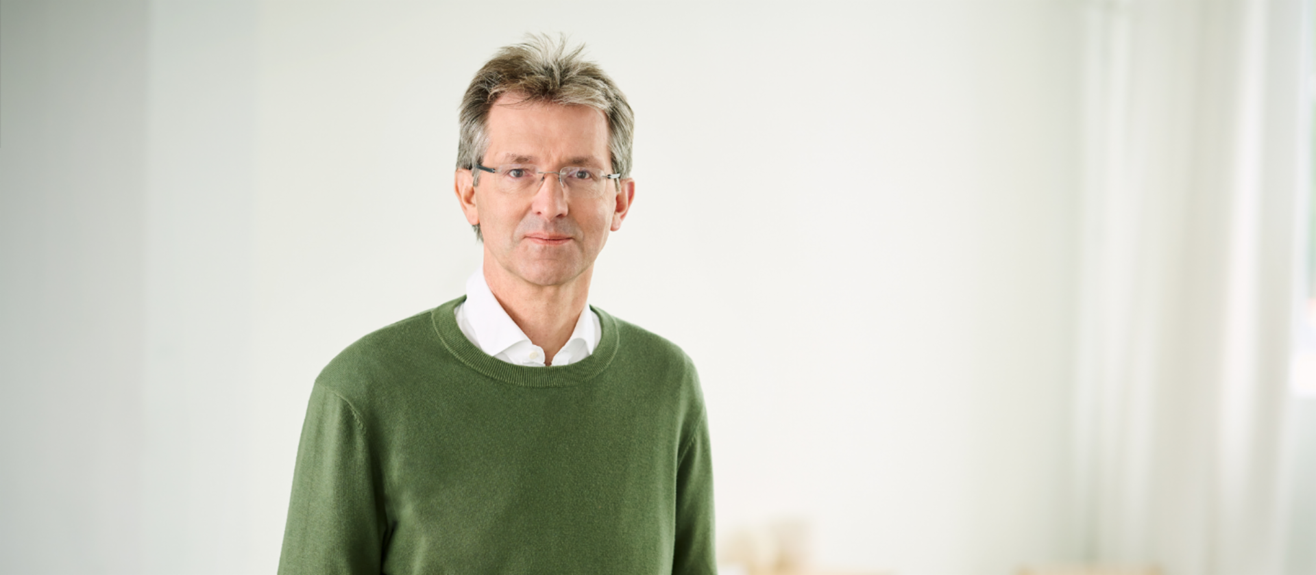 Justus Hecking-Veltman, CFO, stojaci v zelenom svetri a bielej košeli vo svetlej miestnosti.