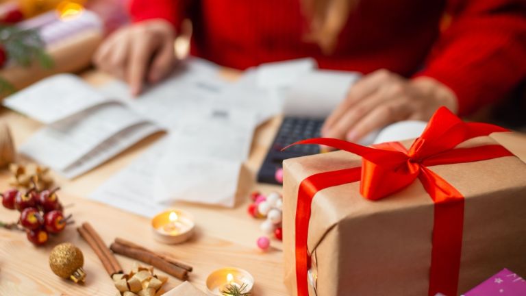 Invoices lay besides Christmas presents at the table. A person sits in front of the table with a red sweater. 
