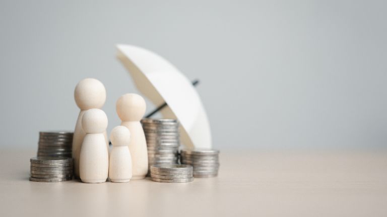 Illustration of four figures standing under an umbrella with stacks of coins around them. 